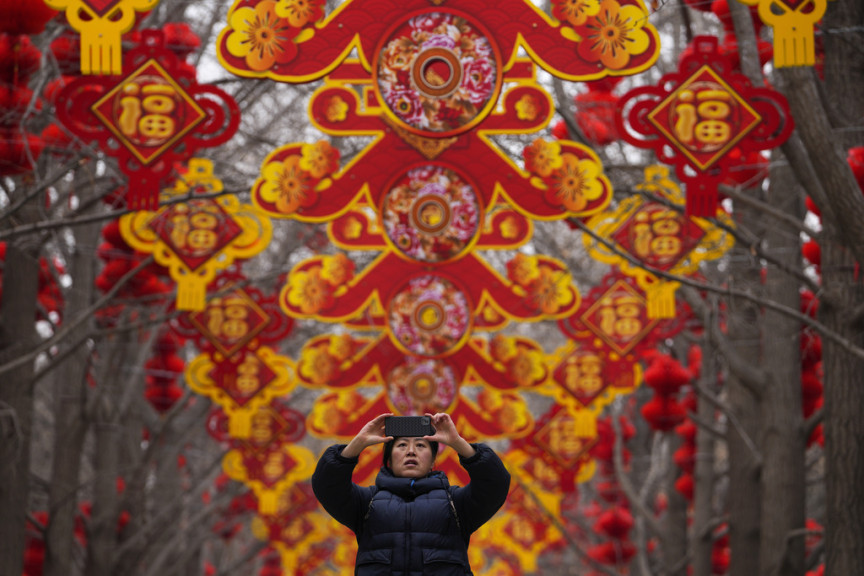 A woman takes a smartphone photo of red lanterns and decorations on display along the trees ahead of the Chinese Lunar New Year at Ditan Park in Beijing, Sunday, Feb. 4, 2024. Chinese will celebrate Lunar New Year on Feb. 10 this year which marks the Year of the dragon on the Chinese zodiac.