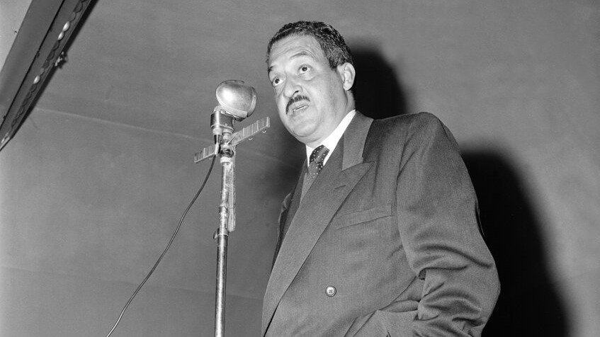 Thurgood Marshall, sporting a mustache and wearing a double-breasted suit, speaks into a public address microphone