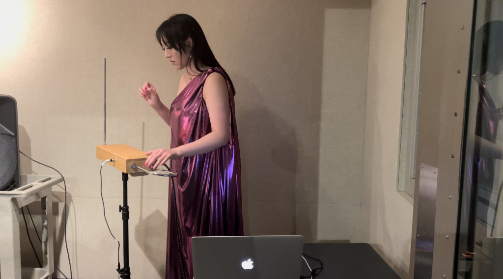 Joy Yang looks down at the theremin while playing, moving her hands in the air very delicately.