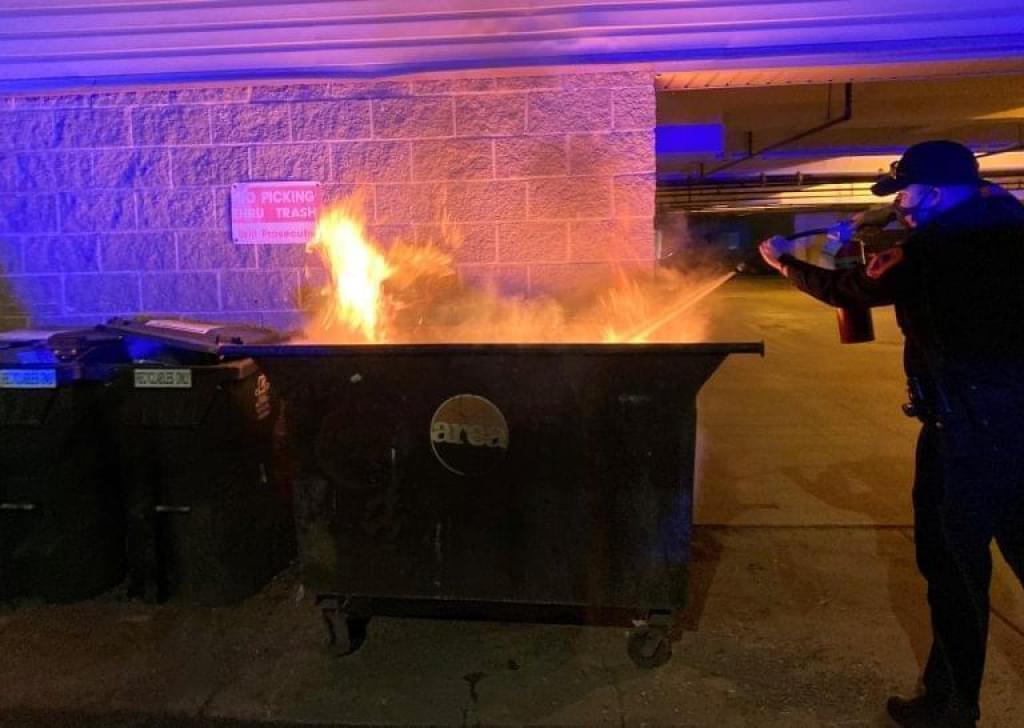University of Illinois Police Officer Kyle Krickovich extinguishes a dumpster fire outside an apartment building in Urbana on Oct. 30, 2020.