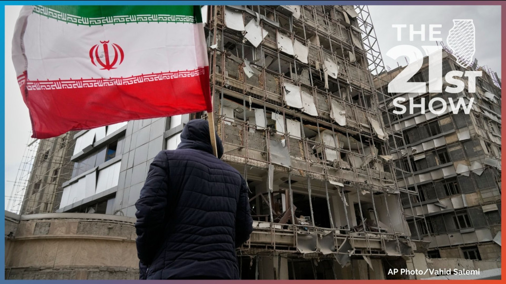 A man holds an Iranian flag as he looks at the damaged façade of Gandhi Hospital, which was hit Sunday when a strike also struck a state TV communications tower and nearby buildings across the street during the ongoing joint U.S.–Israeli military campaign in Tehran, Iran, Monday, March 2, 2026.