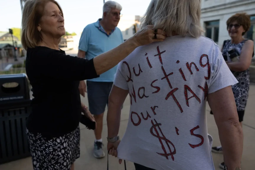Sue Betts, left, 71, helps friend Sheri Schuler-Faust, 69, tuck her scarf into her collar so her message of “quit wasting our tax $’s” can be more easily read on Wednesday after a Madison County Board meeting in Edwardsville.