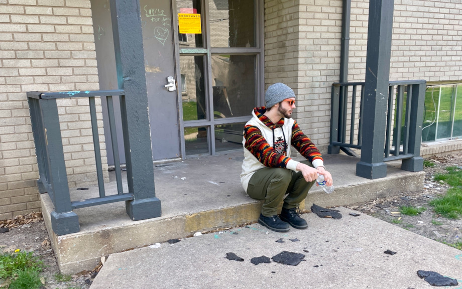 Dustin Schingl sits outside of a condemned building at Champaign Park Apartments in Champaign, Illinois, on April 10. The ground is scattered in broken shingles that fell from the roof.