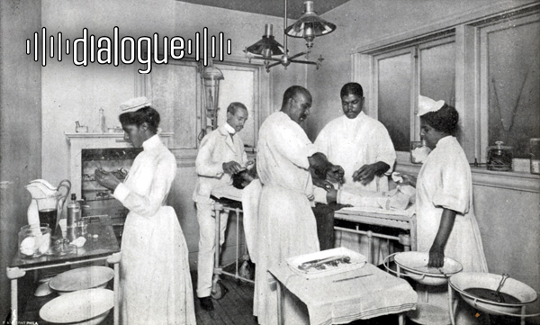 In a black and white photo, Black physicians and nurses hold various medical items and istruments around a patient laying down. One nurse is separated from the rest, near liquid containers. The logo for Dialogue is placed on the top left corner of the photo.