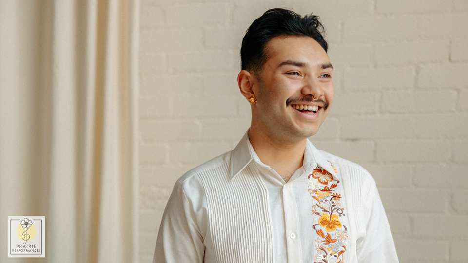 A man in a white button-up shirt with embroidered flowers smiles.