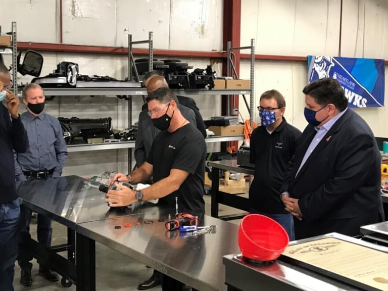 Gov. JB Pritzker looks on Thursday as Heartland Community College/Rivian instructor Tony Foos disassembles part of an electric vehicle at the college's temporary program headquarters in Bloomington.
