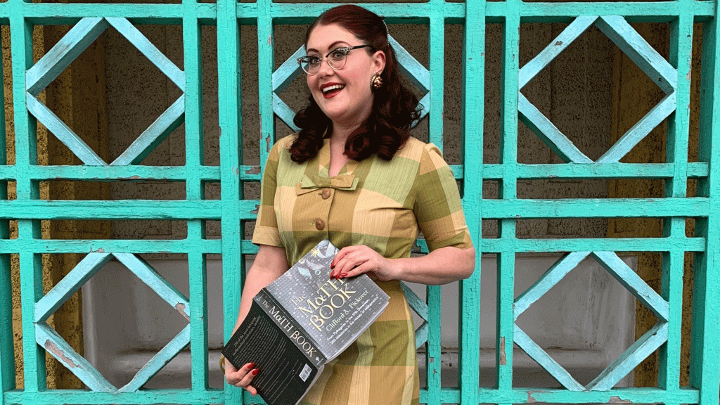woman stands in front of teal metal wall holding a book