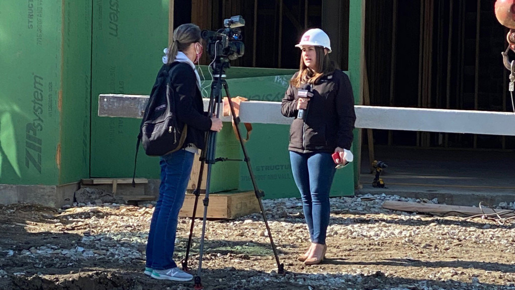 one person behind the camera and one in front of the camera with a microphone and hard hat