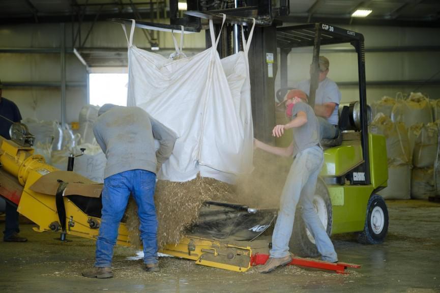 Workers at Shining Star Hemp Co. load a bag of hemp biomass into the processor.
