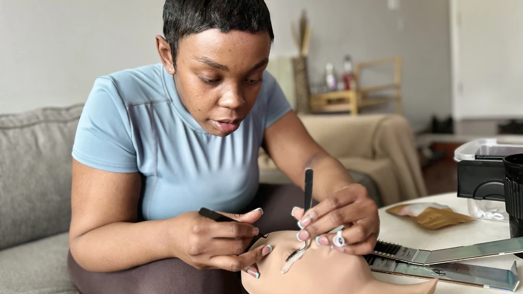 A lash tech puts fake lashes on a mannequin head to practice. 