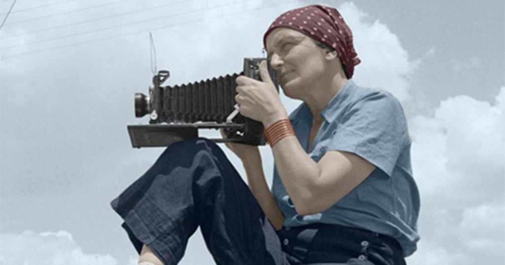 Image of a woman from the first half of the 20th century taking a photograph while sitting atop a car