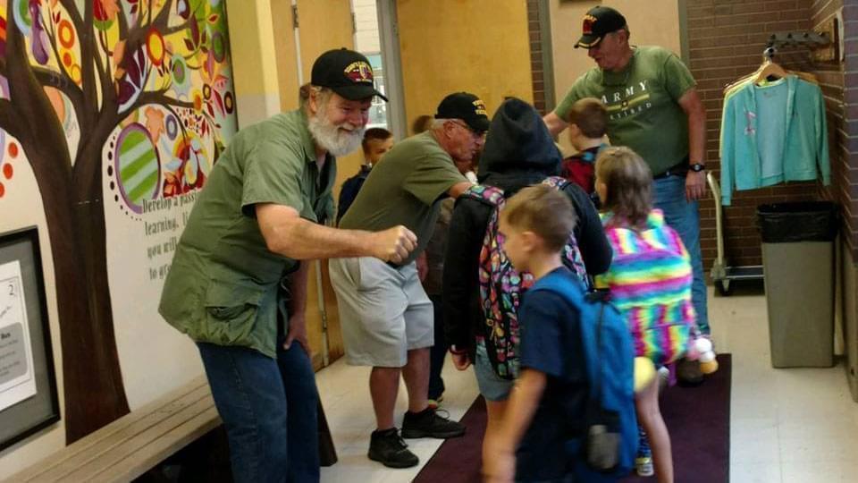 Rick Otey and other veterans greet elementary school children after class. 