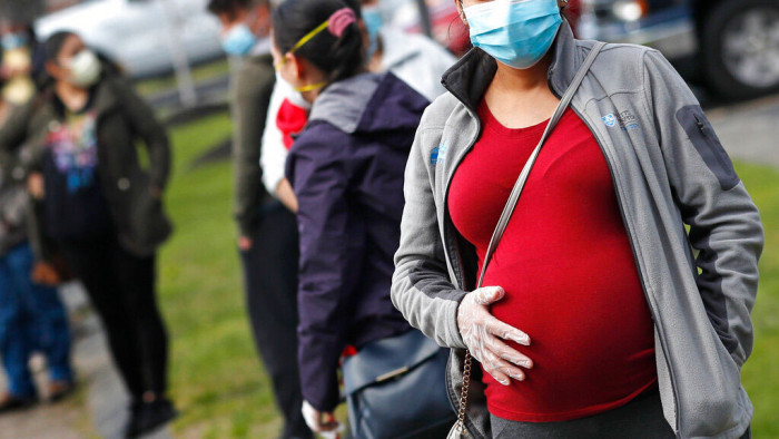 In this May 7, 2020 file photo, a pregnant woman waits in a food pantry line at St. Mary's Church in Waltham, Mass., for people in need of groceries due to the COVID-19 pandemic. Two obstetricians' groups--The American College of Obstetricians and Gynecologists and the Society for Maternal-Fetal Medicine, are now recommending COVID-19 shots for all pregnant women, citing concerns over rising cases and low vaccination rates.