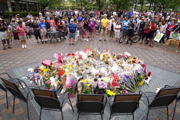 Local residents stand for a two-minute moment of silence at 10:14 a.m. at a memorial Monday, July 11, 2022, in Highland Park, Ill., to the seven people who lost their lives during the town's Fourth if July parade. 