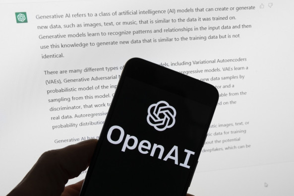 The OpenAI logo is seen on a mobile phone in front of a computer screen displaying output from ChatGPT, March 21, 2023, in Boston. 