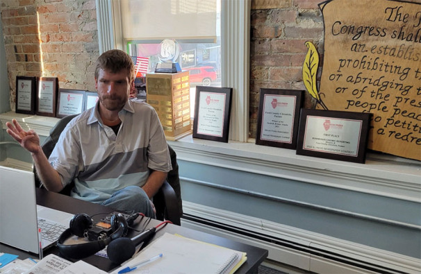 News editor and co-publisher Will Brumleve sits at his desk at the Ford County Chronicle in front of awards and text from the First Amendment. He and co-founder Andrew Rosten launched the newspaper in Paxton, Illinois, in 2020, one of the few new papers in the U.S. in recent years.