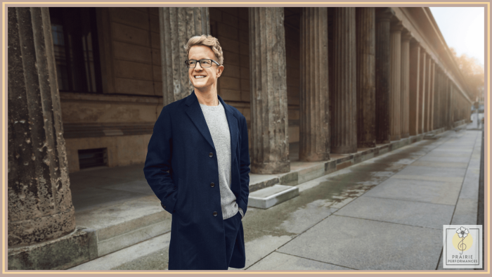A blonde man in glasses standing on a street. 