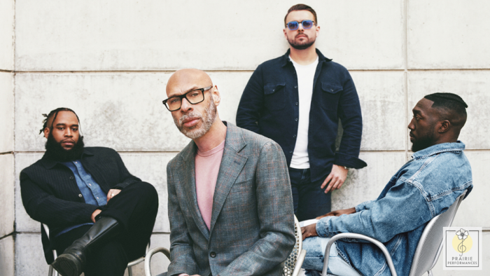 The four members of the Joshua Redman Quartet. Three are sitting relaxed in chairs, and one is leaning against a wall wearing sunglasses. 