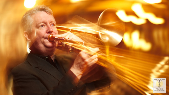 A white man with gray hair in a dark suit playing trombone so fast that the instrument looks blurry.