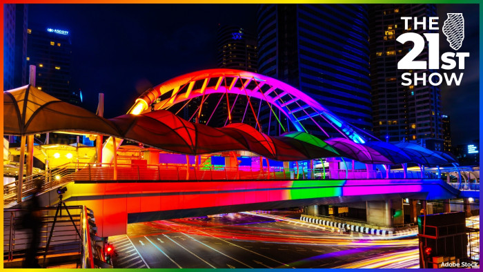 a long-exposure image of a bridge lit up in the rainbow colors of the pride flag as the lights of vehicles streak underneath