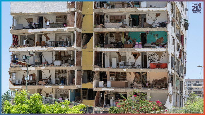 a white building has one wall complete missing, giving it a horrible doll-house appearance; inside you can see six floors' worth of people's lives: kitchen appliances, tables and chairs, and a painting of a tree and birds on a wall above an orange sofa