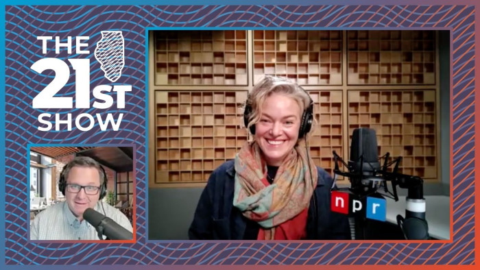 a white woman with blond hair wearing a black top and colorful scraf; she sits behind a broadcast microphone with an NPR logo, in front of a grid of honey brown sound-dampening squares on the wall of the studio