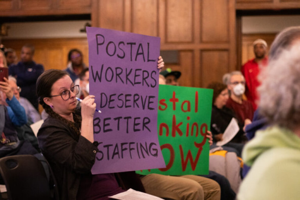 Protestors against the Post Office changes holding up signs at the public input meeting hosted by the US Postal Service on Tuesday, March 12 at the University of Illinois' YMCA. 