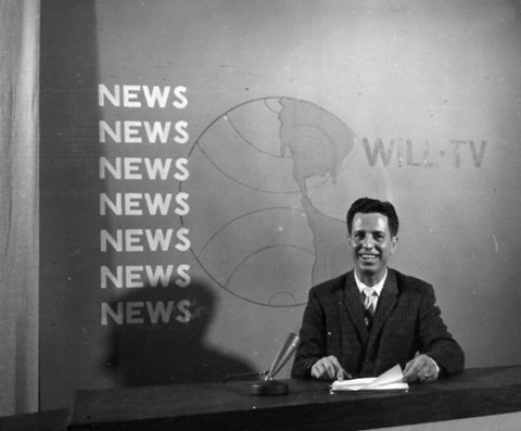 man sit behind news desk on tv set
