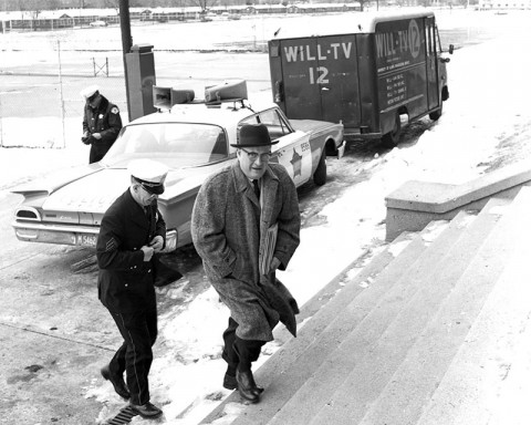 man walks up steps with a police car and WILL-TV van in background