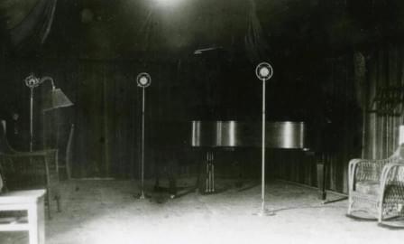 The main studio of WRM Radio (soon to be renamed WILL) on the University of Illinois campus, circa 1927. A piano was a common feature in an era when most music on the radio was live. The spring microphones of the time were designed to prevent undesired vibrations or feedback. Draperies lined the walls to improve acoustics.