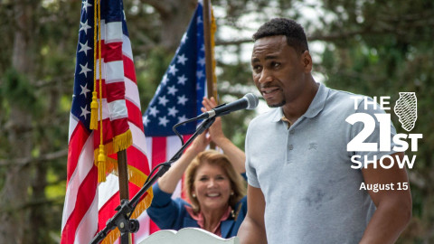 man talks at microphone while woman cheers