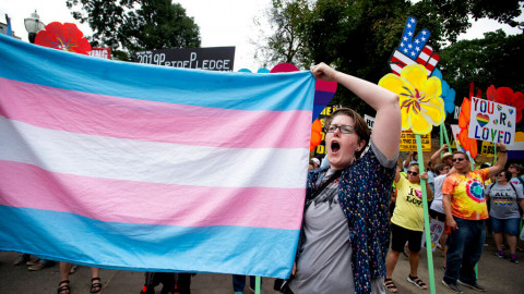 A supporter for the transgender community holds a trans flag in front of counter-protesters to protect attendees from their insults and obscenities at the city's Gay Pride Festival in Atlanta on Saturday, Oct. 12, 2019.