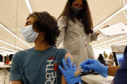 Kieran Layland, 15, receives his first Pfizer COVID-19 vaccination as his mother, Ashlesha Patel, observes from behind at the Cook County Public Health Department, Thursday, May 13, 2021, in Des Plaines, Ill.