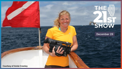 two women and a man smile for a photo on a catamaran sailboat boat during a break from an interview; a wooden crate, multiple cameras on tripods, and the ship's rigging can be seen