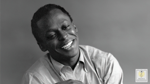 Miles Davis smiles, looking relaxed with his head tilted to the side.