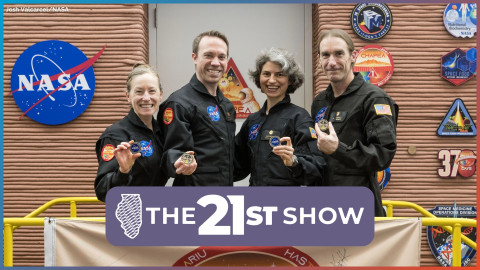 Four people in navy blue flight suits show off medals commemorating their simulated mission to mars. They are standing in front of an adobe-colored building adorned with the logos of NASA and subsidiary space research projects