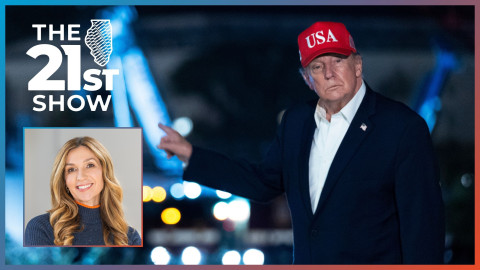 President Trump is wearing a dark-blue suit, white button-down shirt and red USA hat; he looks toward the camera and points behind him; the image was taken at night, so the construction project appears out of focus as a series of color blobs in the background. Amanda Carpenter, in an inset photo, is a white woman with blond-brown hair, wearing a navy blue turtleneck sweater flecked with white and featuring an orange ring around the top of the collar.