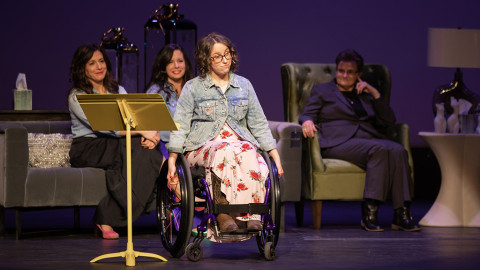 woman in wheelchair on stage with people sitting on couches behind her