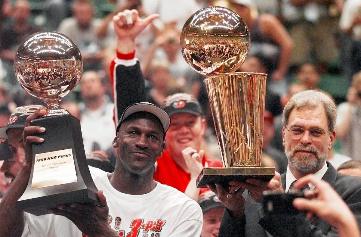 Chicago Bulls’ Michael Jordan, left, holds the Most Valuable Player trophy as coach Phil Jackson holds the NBA Championship trophy after the Bulls defeated the Utah Jazz 87-86 in Game 6 of the NBA Finals in Salt Lake City, Sunday, June 14, 1998. 